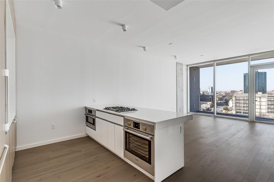 A well-lit kitchen island with built-in appliances and a city view through large windows. A well-lit kitchen island with built-in appliances and a city view through large windows.