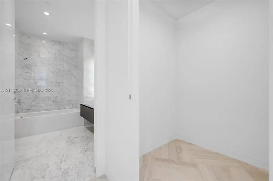 Bathroom featuring stone-finish wall and floor tiling, a soaking tub with integrated shower hardware, a floating vanity with a vessel sink, and herringbone-pattern wood-finish flooring