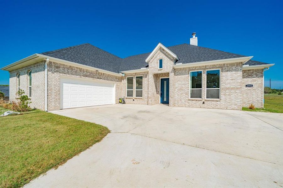 View of front of home featuring a shingled roof, a front yard, driveway, brick siding, and an attached garage View of front of home featuring a shingled roof, a front yard, driveway, brick siding, and an attached garage
