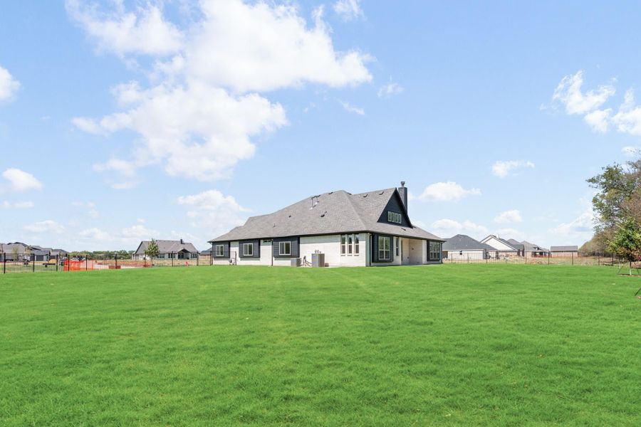 Rear view of single-story home with dark roof, white and gray exterior, and large fenced backyard