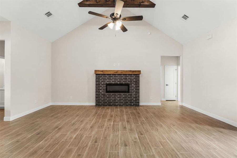 Unfurnished living room featuring high vaulted ceiling, a tiled fireplace, ceiling fan, and light wood-style flooring