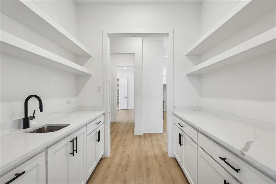 Bar featuring sink, white cabinets, light stone counters, and light hardwood / wood-style floors