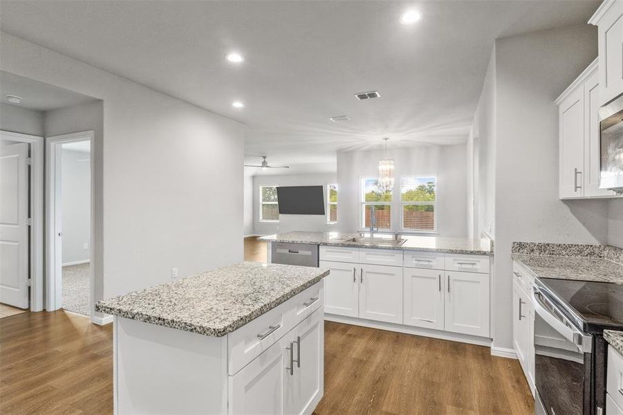 Kitchen with a kitchen island, light stone countertops, wood-type flooring, sink, and white cabinetry