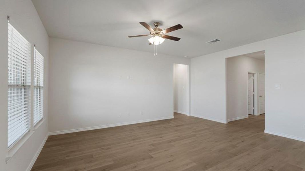 Spacious room featuring wood-finish flooring, white walls, and a ceiling fan with integrated lighting