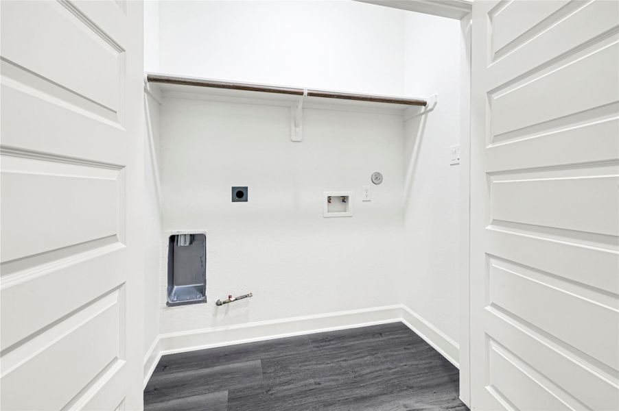 This is a bright, compact laundry room with hookups for a washer and dryer. It features a shelf for storage and has sleek, dark flooring contrasting with white walls. This is a bright, compact laundry room with hookups for a washer and dryer. It features a shelf for storage and has sleek, dark flooring contrasting with white walls.