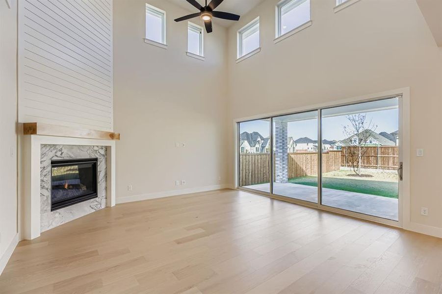 Unfurnished living room with a fireplace, a towering ceiling, light wood-style flooring, and a ceiling fan