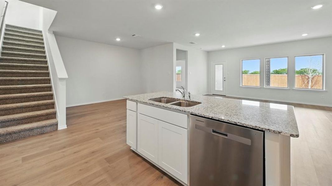 Kitchen featuring stainless steel dishwasher, white cabinetry, light stone countertops, open floor plan, and light wood-type flooring