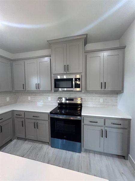 Kitchen with gray cabinetry, range, stainless steel microwave, and decorative backsplash Kitchen with gray cabinetry, range, stainless steel microwave, and decorative backsplash