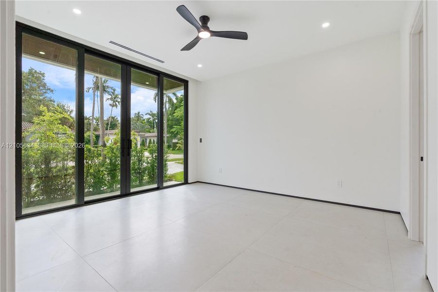 Large-format tile flooring, multi-panel sliding glass doors with dark frames, matte black ceiling fan, and recessed lighting