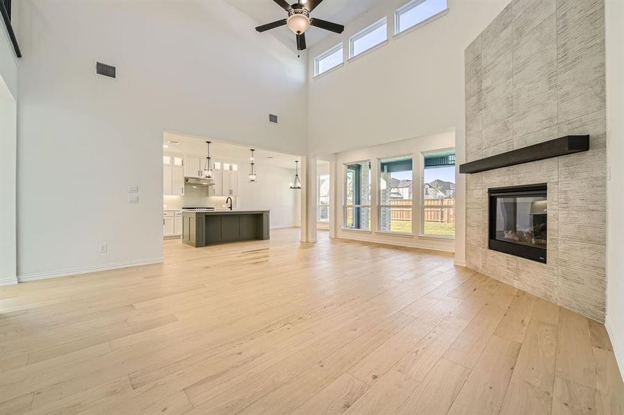 Unfurnished living room featuring light hardwood / wood-style flooring, a healthy amount of sunlight, a high ceiling, and a tile fireplace