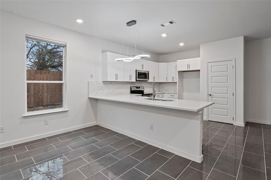 Kitchen with white cabinetry, hanging light fixtures, stainless steel appliances, and kitchen peninsula