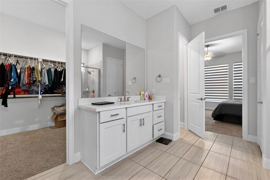 Bathroom featuring a spacious closet, vanity, light colored carpet, a shower stall, and light tile patterned floors