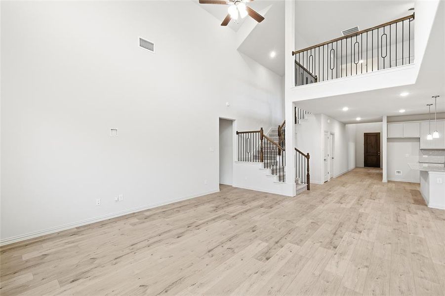 Unfurnished living room with light wood-type flooring, recessed lighting, ceiling fan, stairs, and a towering ceiling