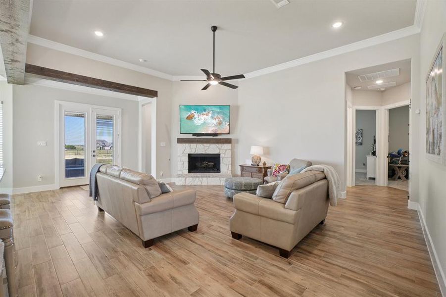 Living room with crown molding, light wood-look ceramic tile flooring, a stone fireplace, a ceiling fan, and recessed lighting