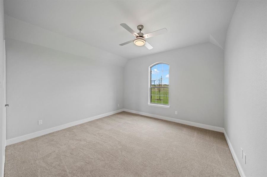 Carpeted spare room featuring vaulted ceiling and ceiling fan