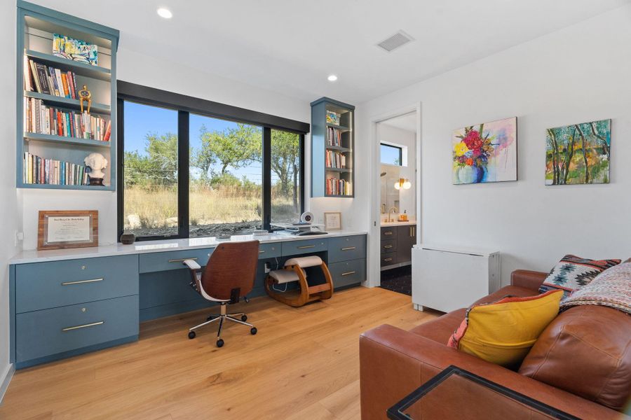 Dedicated office space featuring expansive window, built-in cabinetry, integrated shelving, light wood-finish flooring, and recessed ceiling lighting