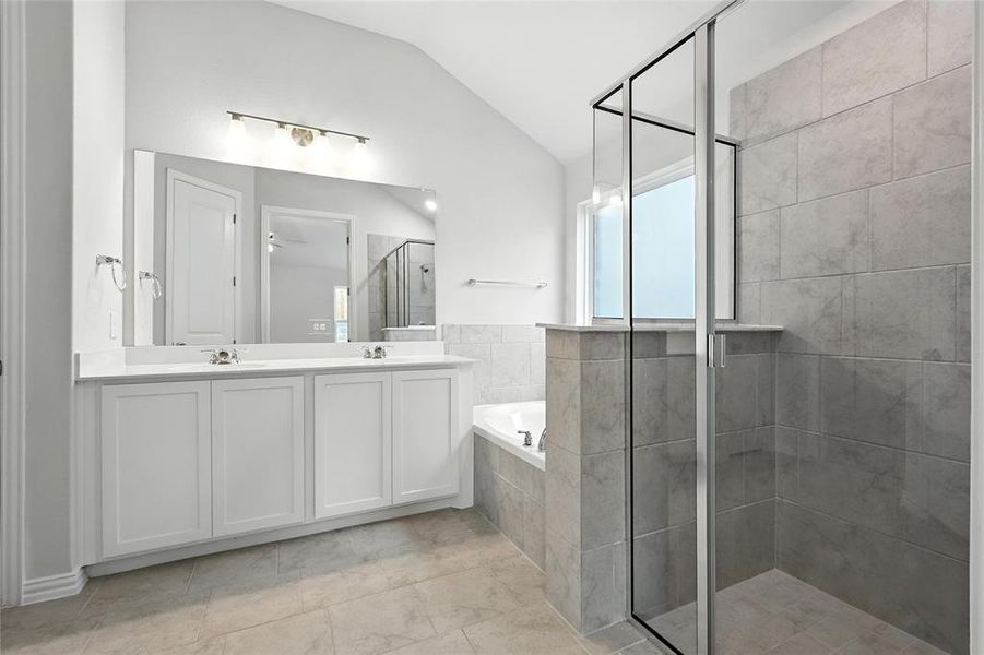 Bathroom with a stall shower, lofted ceiling, double vanity, a garden tub, and light tile patterned flooring