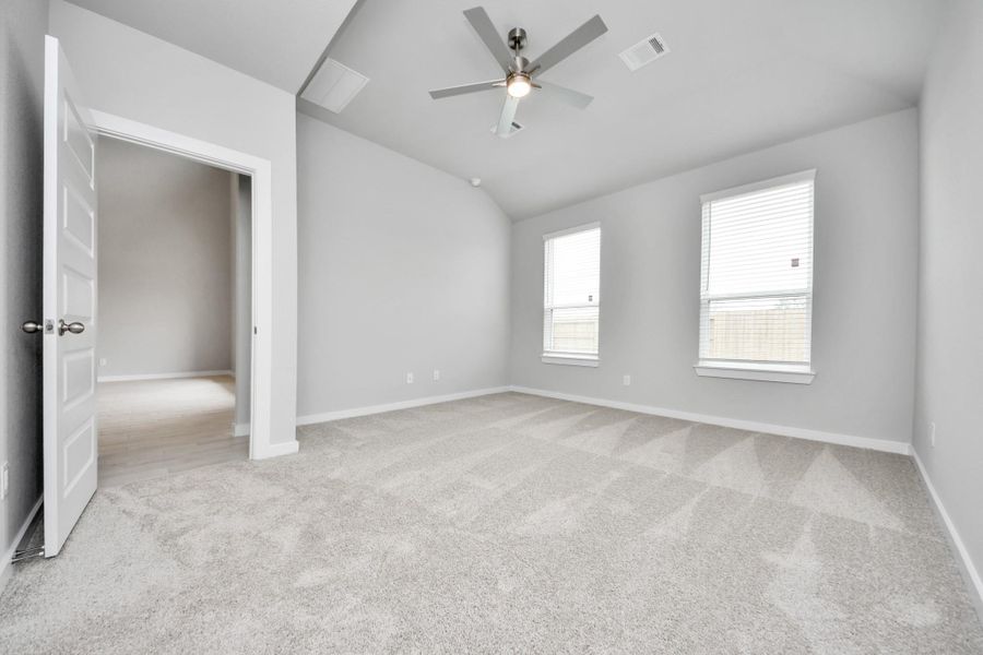 Escape and relax in the exquisite primary suite, a haven to unwind after a long day. The spacious room, located on first floor, boasts plush carpeting, soothing paint tones, high ceilings, and expansive windows adorned with privacy blinds. Sample photo of completed home with similar floor plan. Actual colors and selections may vary.