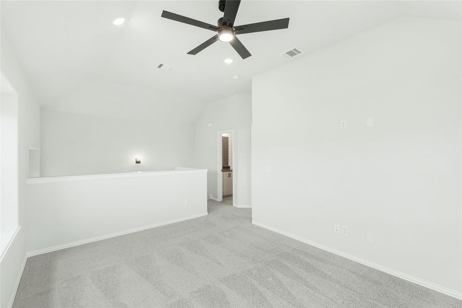 Empty bedroom with vaulted ceiling, ceiling fan, gray carpet, and half-wall divider leading to ensuite bathroom