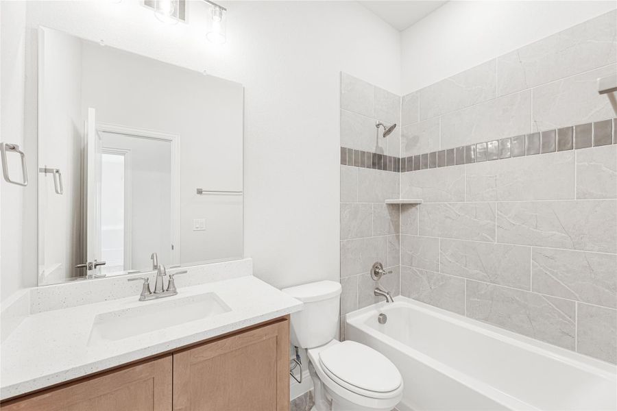 Bathroom with quartz vanity, wood cabinets, and tiled tub-shower combo with decorative accent strip Bathroom with quartz vanity, wood cabinets, and tiled tub-shower combo with decorative accent strip