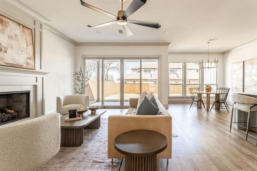 Living area featuring crown molding, ceiling fan, a tiled fireplace, light wood-style floors, and hanging lights