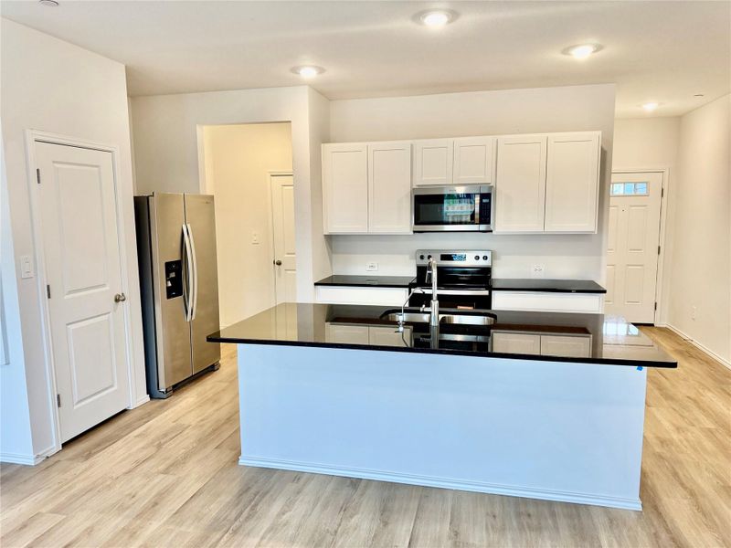 Kitchen featuring white cabinetry, stainless steel appliances, light wood-style floors, dark stone countertops, and an island with sink
