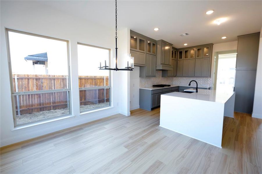 Kitchen featuring an island with sink, a chandelier, light wood-style flooring, gray cabinets, and recessed lighting Kitchen featuring an island with sink, a chandelier, light wood-style flooring, gray cabinets, and recessed lighting