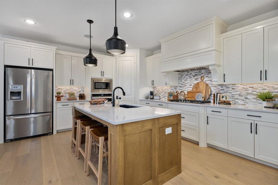 Kitchen with an island with sink, light stone countertops, white cabinets, pendant lighting, and appliances with stainless steel finishes