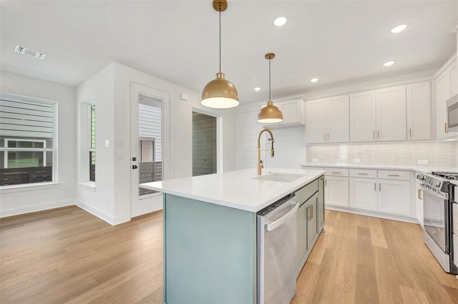 Open-concept kitchen featuring light wood-finish flooring, a central island with a white countertop, two pendant light fixtures, white cabinetry, and stainless steel appliances