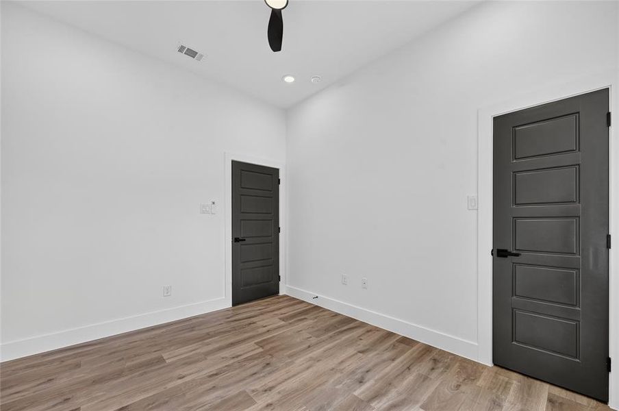 Room featuring neutral white walls, wood-finish flooring, and two paneled doors with matte black hardware Room featuring neutral white walls, wood-finish flooring, and two paneled doors with matte black hardware