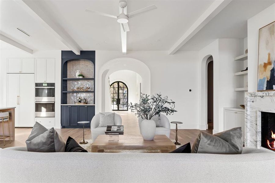 Living area featuring built in shelves, beam ceiling, arched walkways, a fireplace, and a ceiling fan Living area featuring built in shelves, beam ceiling, arched walkways, a fireplace, and a ceiling fan