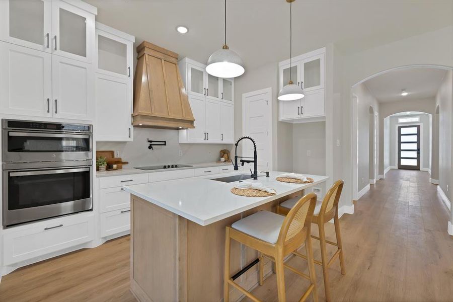 Kitchen featuring custom range hood, stainless steel double oven, arched walkways, a sink, and black electric stovetop Kitchen featuring custom range hood, stainless steel double oven, arched walkways, a sink, and black electric stovetop