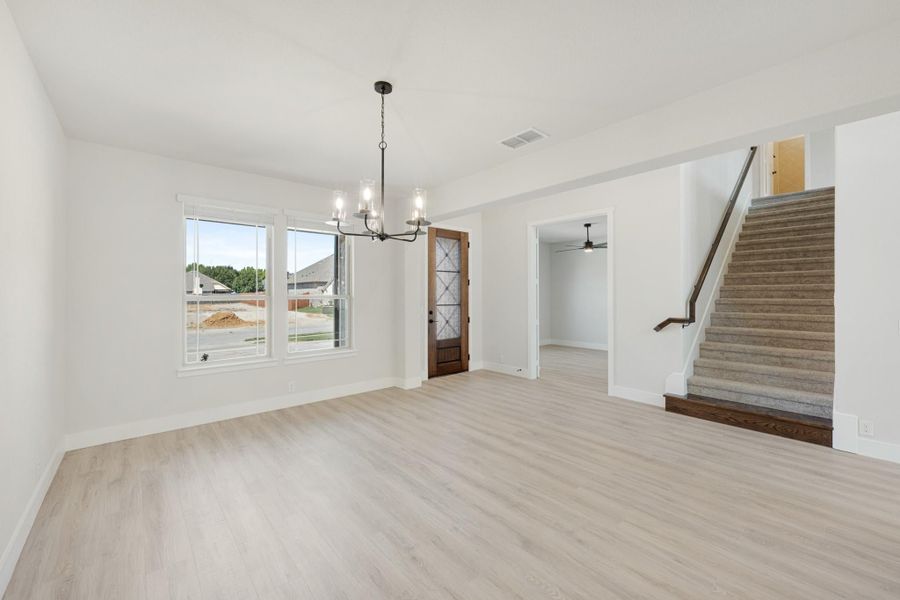 Open dining area with light wood floors, chandelier, and carpeted staircase nearby
