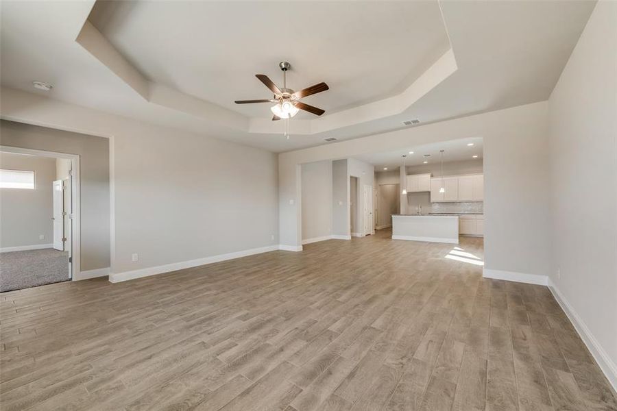 Unfurnished living room with ceiling fan, a tray ceiling, and light wood-type flooring