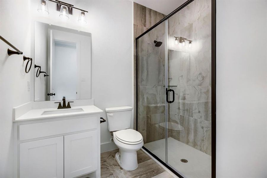 Contemporary bathroom featuring a frameless glass shower enclosure with matte black hardware, a white single vanity with a quartz countertop, and large format tile flooring Contemporary bathroom featuring a frameless glass shower enclosure with matte black hardware, a white single vanity with a quartz countertop, and large format tile flooring