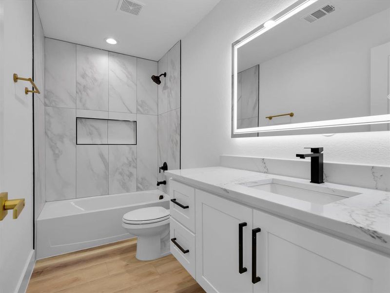 Full bathroom featuring vanity, hardwood / wood-style floors, tiled shower / bath combo, and toilet