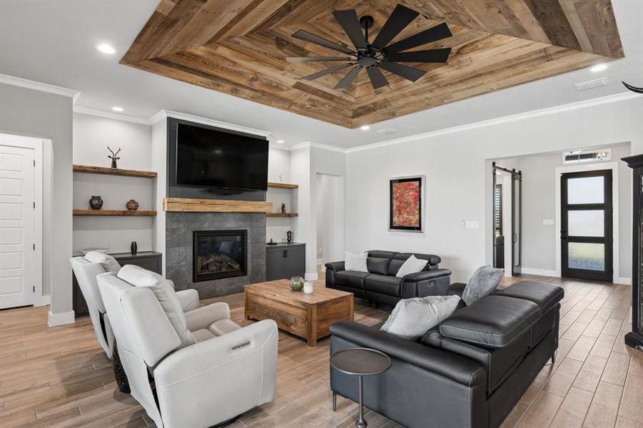 Living room with a barn door, crown molding, a tile fireplace, light wood finished floors, and a raised ceiling
