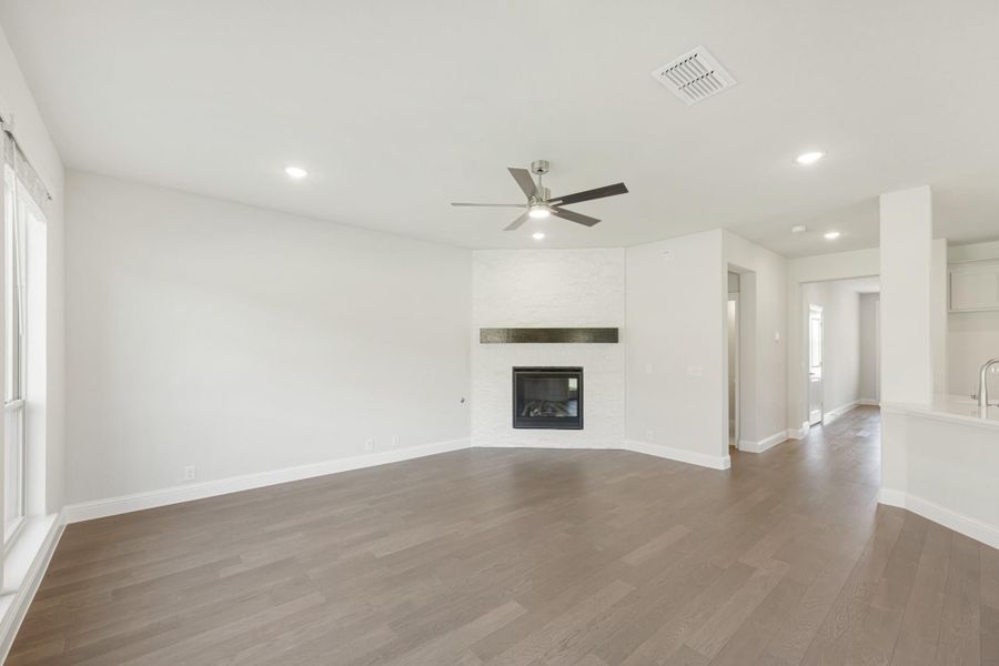 Open living room with hardwood floors, white brick fireplace, and ceiling fan