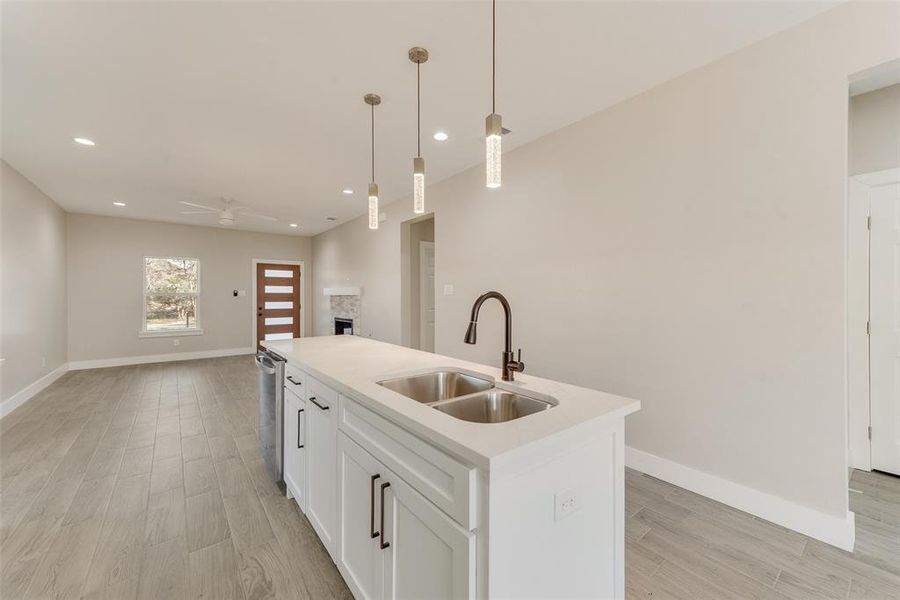 Kitchen with pendant lighting, white cabinetry, an island with sink, dishwasher, and sink