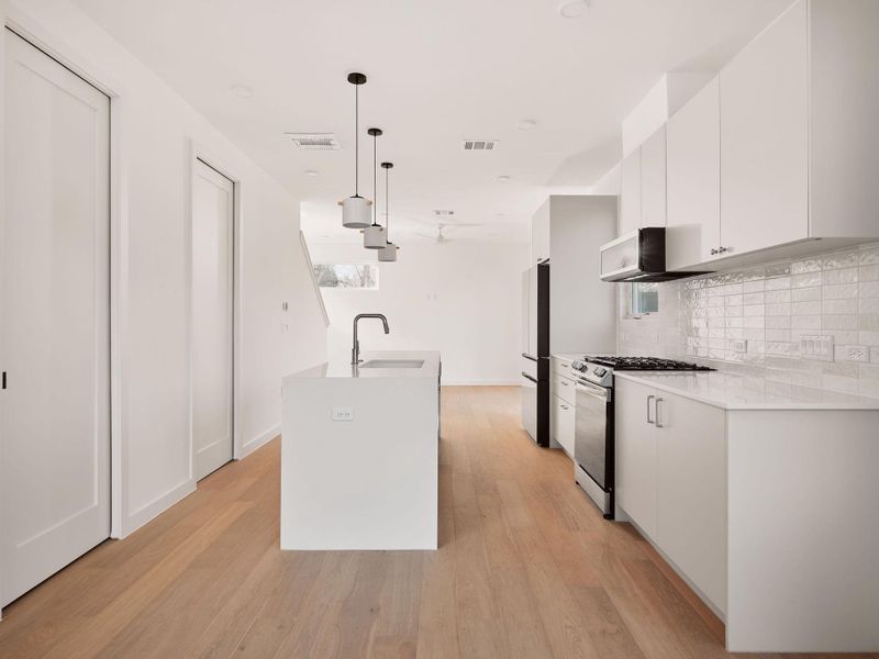 Kitchen featuring hanging light fixtures, gas stove, white cabinets, and modern cabinets