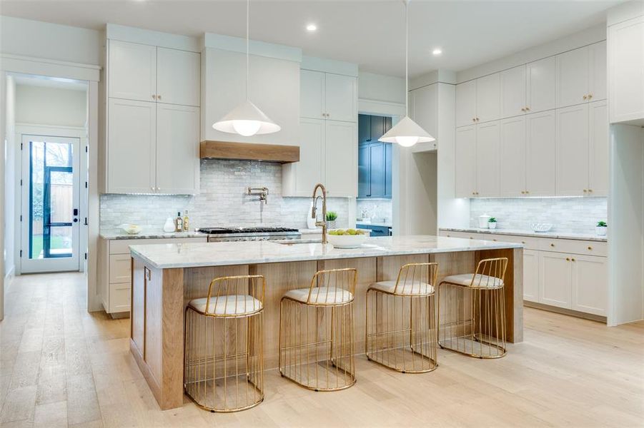 Kitchen with white cabinetry, light stone counters, and a center island with sink