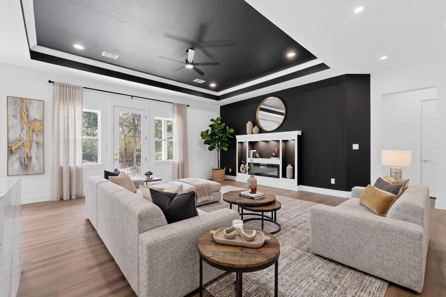 Recessed lighting illuminates this inviting living space with a distinct tray ceiling and sleek flooring.