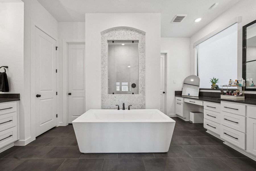 The spa-like primary ensuite with modern freestanding tub, walk-in shower, and conveniently placed dueling vanities, hers with a makeup area.