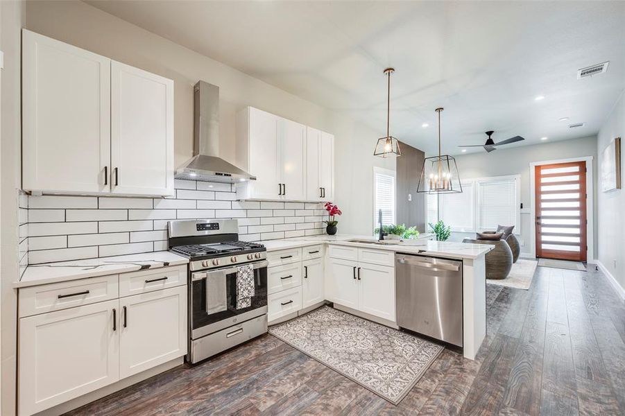 Kitchen featuring stainless steel appliances, wall chimney exhaust hood, white cabinets, backsplash, and recessed lighting