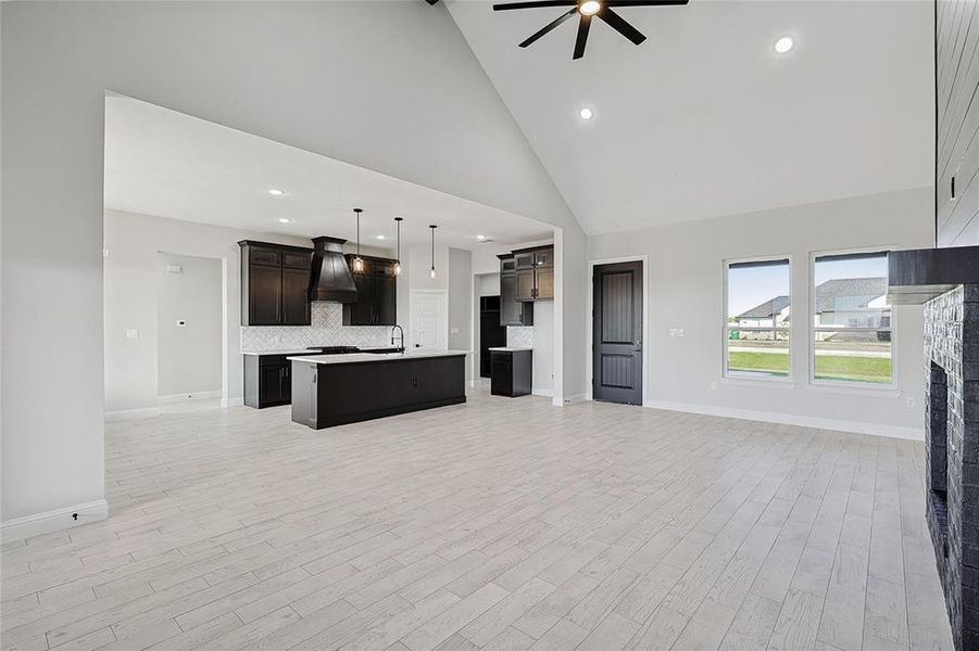 Unfurnished living room with light hardwood / wood-style flooring, high vaulted ceiling, ceiling fan, and sink