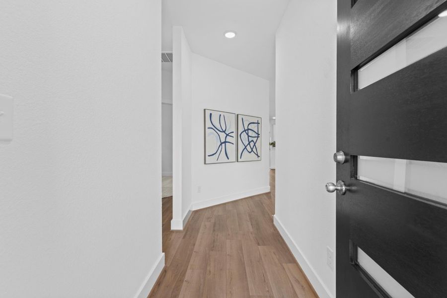 Modern custom dark charcoal gray front door opens to a bright and inviting entryway with wood look vinyl flooring, high ceilings, and clean lines—setting the tone for stylish, comfortable living. **Image Representative of Plan Only and May Vary as Built**.