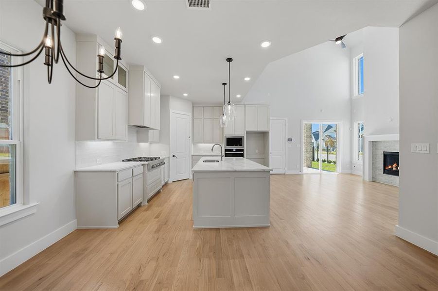 Kitchen featuring an island with sink, light wood-style flooring, open floor plan, recessed lighting, and a glass covered fireplace