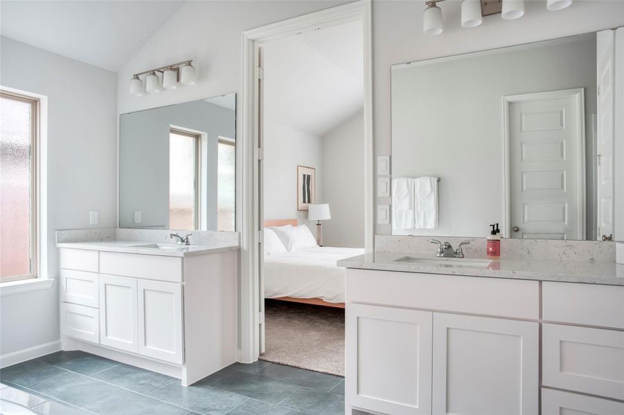 The photo shows a bright, modern bathroom with dual sinks, large mirrors, and sleek white cabinetry. It connects to a bedroom with a glimpse of a bed and soft carpeting, creating a seamless, elegant space. The photo shows a bright, modern bathroom with dual sinks, large mirrors, and sleek white cabinetry. It connects to a bedroom with a glimpse of a bed and soft carpeting, creating a seamless, elegant space.
