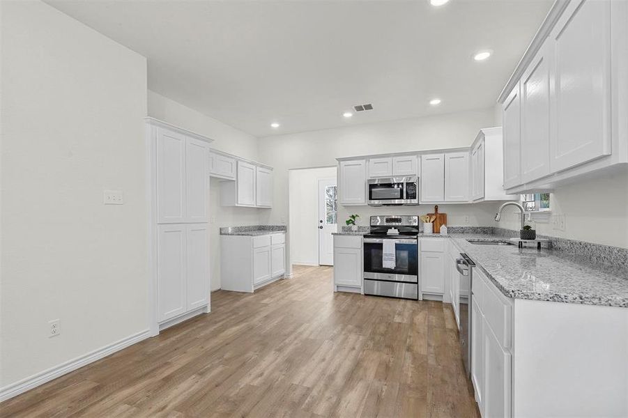 Kitchen with stainless steel appliances, light wood-type flooring, light stone counters, sink, and white cabinetry