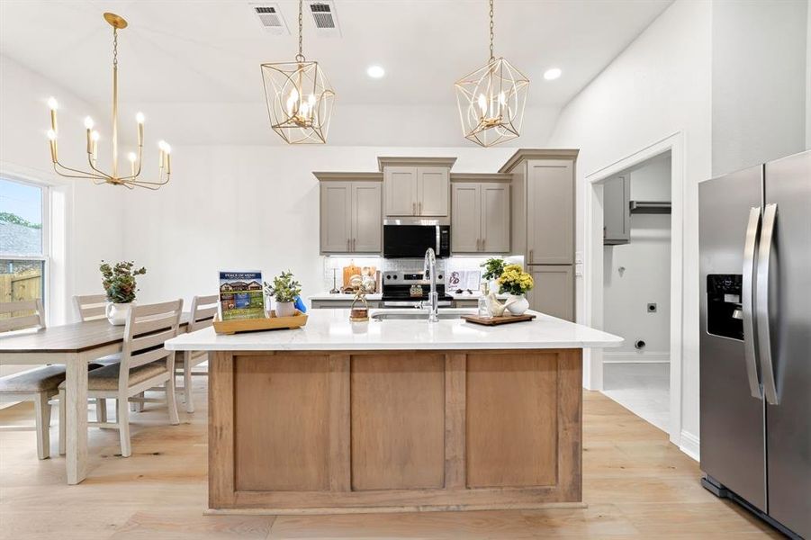 Open-concept kitchen featuring a wood-finish island with a light-toned countertop, gray cabinetry, and stainless steel appliances